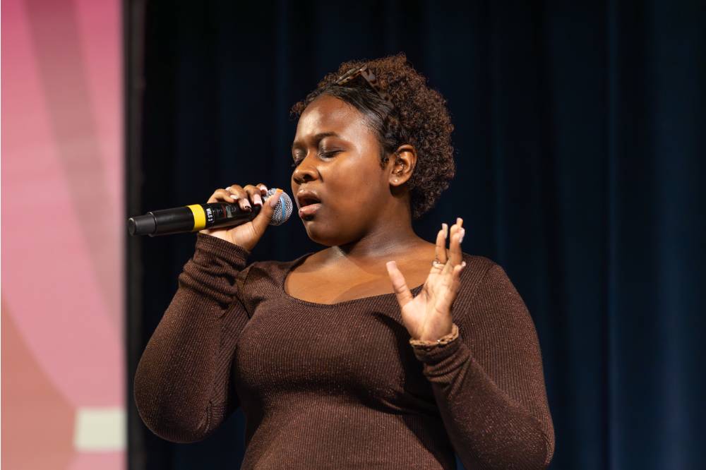 Jaimee Hickson singing into a wireless microphone holding up her hand.